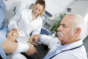 senior doctor is bandaging the arm of his patient