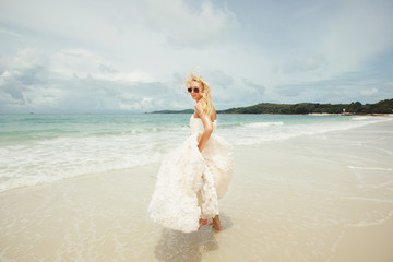 Fototapeta na wymiar young woman in wedding dress goes over sea turning back. bride on the beach.