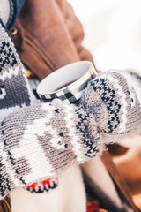 a girl in warm mittens with patterns holds a cup of hot tea in the street in the winter