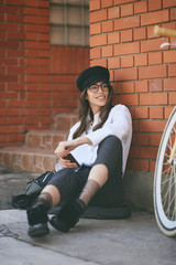 Fototapeta na wymiar Woman sitting on sidewalk and using smart phone. Next to her yellow bicycle.