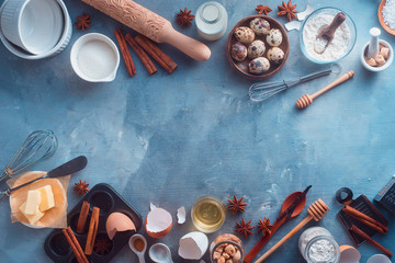 Fototapeta na wymiar Cooking concept with baking tools and ingredients. Muffin tin, rolling pin, whisk, honey spoon, milk bottle, butter, sugar, flour, cinnamon and eggs on a textured background with copy space