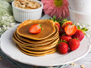 Stack of oatmeal flour pancakes with strawberries on white dish
