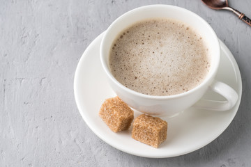 hite coffee Cup and saucer with milk foam and cane sugar on concrete background