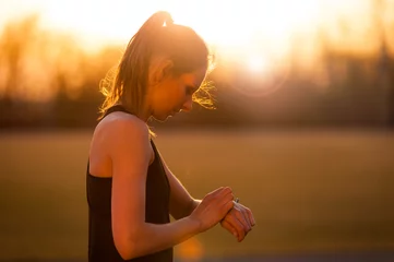 Fotobehang Fitness woman setting up smart watch before running training during sunset © leszekglasner