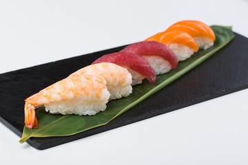 Nigiri sushi served on black stone slate, white background