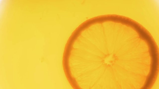 Slow motion video of orange slice slowly rotating in juice jar