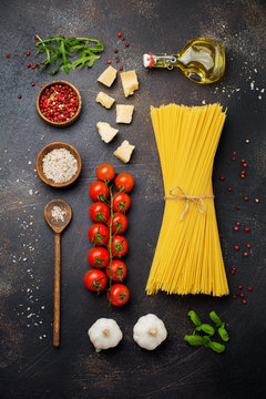 Ingredients for traditional Italian pasta dish.Raw spaghetti, parmesan cheese, olive oil, garlic, basil leaves, pepper, cherry tomatoes on old dark stone background.   Top view.