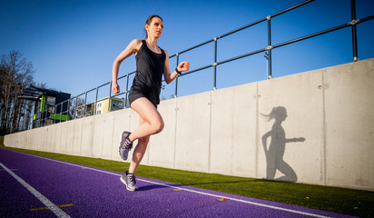 Fototapeta na wymiar Athletic woman running on stadium track during sunny day