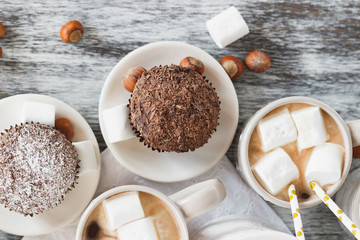 Cups with cacao and marshmallow, cupcakes and different decorations
