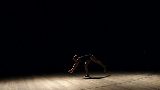 A flexible girl does a gymnastic somersault on a stage performance in the dark, a slow movement.