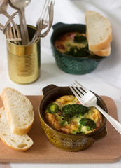 Baked scrambled eggs with broccoli, sausages and cheese served with slices of bread. Rustic style.
