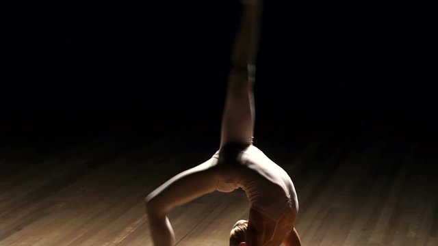 Very young ballerina posing on a black background. Young teenage girl dancing ballet on stage in the dark, slow motion.