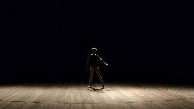 A small talented girl makes a gymnastic somersault on stage in the dark with the light of concert lighting and smoke.
