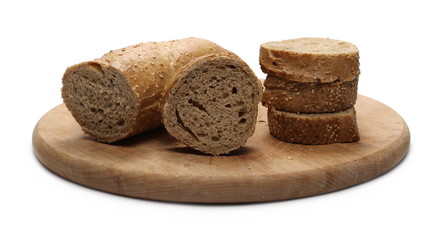 Loaf of whole wheat bread with sesame and slices on round wooden cutting board isolated on white background