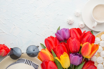 Multicolored tulips with coffee, hat, glasses, and a bise on a light background, top view, with empty space for writing or advertising