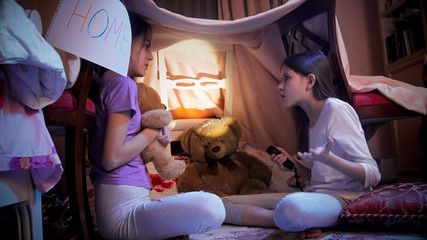 Obraz na płótnie Canvas Teenage girls with flashlight talking in selfmade tent at bedroom