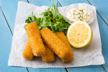 crispy fried fish fingers with lemon and sauce on blue wooden background