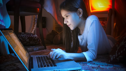 Portrait of smiling girl in bedroom using social media on laptop at night