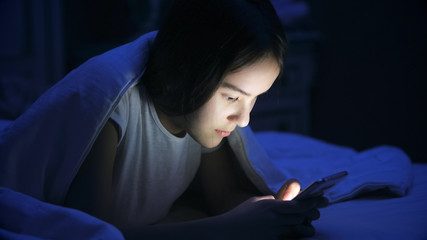 Portrait of teenage girl lying in bed at night and using smart phone