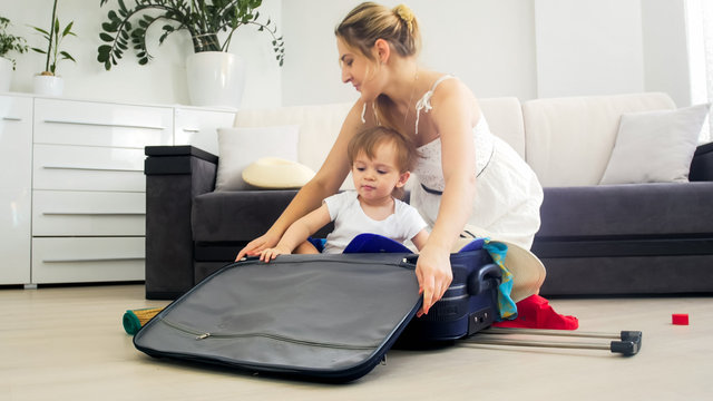 Beautiful young mother and toddler boy packing suitcase for holidays