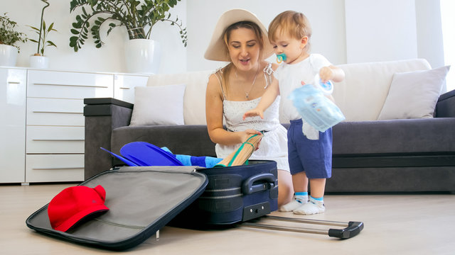 Beautiful young mother with toddler boy packing suitcase for vacation