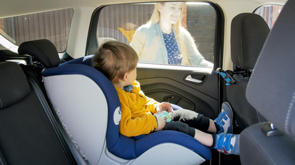 Cute toddler boy sitting in safety car seat