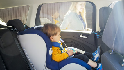 Cute toddler boy sitting in car safety seat