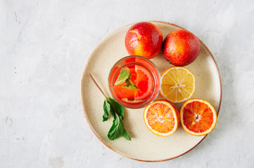 Glass of citrus infused water with mint. Blood oranges and lemon in a plate on a white background. Top view and copy space.