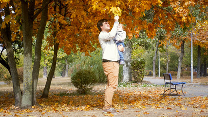 Happy smiling father holding his toddler son in autumn park at bright sunny day