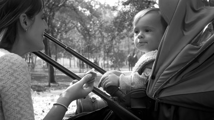 Black and white portrait of cute toddler boy eating in stroller at park