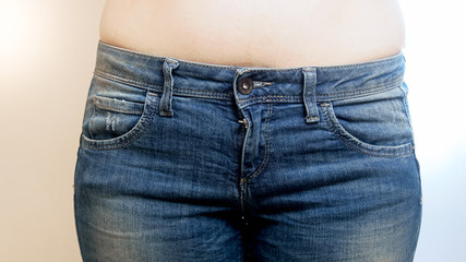 Closeup photo of young woman with naked belly and blue jeans