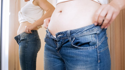 Closeup photo of young woman with big belly wearing tight jeans at mirror