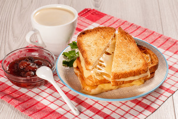 Toasted slices of bread with cheese and green parsley on white plate, cup of coffee, spoon and bowl with strawberry jam on napkin