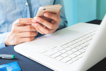 Fototapeta premium Close up image of woman's hands using smartphone and laptop computer on workspace desk, Space for text or design