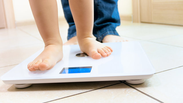 Closeup image of baby's feet standing on digital weight scales