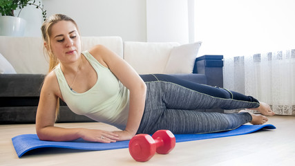 Beautiful young woman lying on fitness mat at home