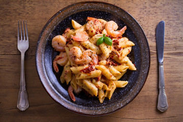 Shrimp penne with sun dried tomatoes and basil in creamy mozzarella sauce. Pasta with shrimps in bowl on wooden table. overhead, horizontal