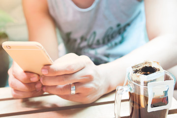 Hands of man using smartphone with drip coffee on wooden table, Technology and lifestyle concept