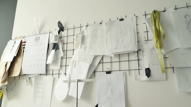 Clothing design sketches, black and white templates and drawings pinned on white wall in studio. Planning new clothes collection and creative thinking concept.