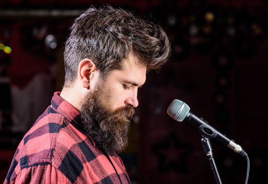 Talented vocalist concept. Musician, vocalist with beard and mustache lighted by spotlight. Man on calm face holds microphone, singing lyric song, black background, copy space.