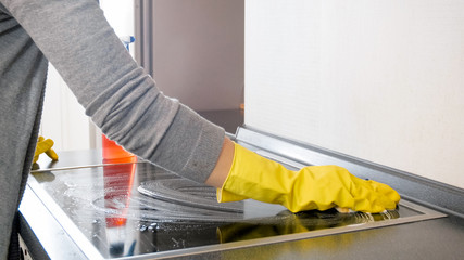 Closeup photo of young woman applying cleaning detergent on electric hob