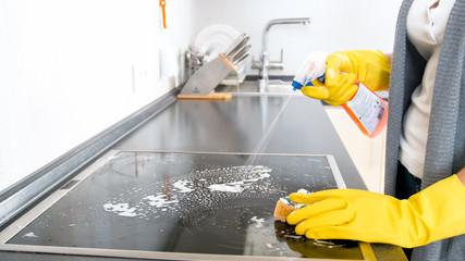 Closeup image of young housewife using detergent spray to clen electric hob