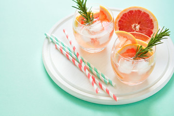 Refreshment grapefruit cocktail with rosemary on white wooden board. Healthy citrus summer drink. Mint color background