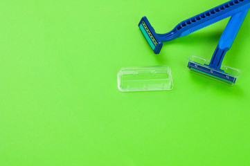 Two new blue plastic disposable razors with two blades and humid strip in transparent cover on blank green paper