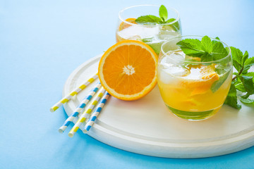 Orange lemonade with slices of orange, ice and mint on blue background.