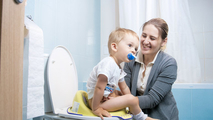 Portrait of smiling young mother teaching her toddler son using toilet