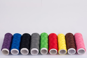 Row of bobbins of new colorful threads on white background