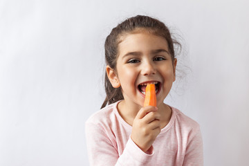 Happy little child girl eating fresh vegetables. Isolated portrait on white background. Healthy teeth.