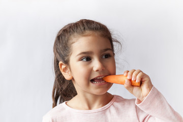 Happy little child girl eating fresh vegetables. Isolated portrait on white background. Healthy teeth.
