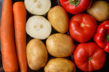 Potatoes, orange carrots, ripe tomatoes, onions and red peppers on a black background, top view